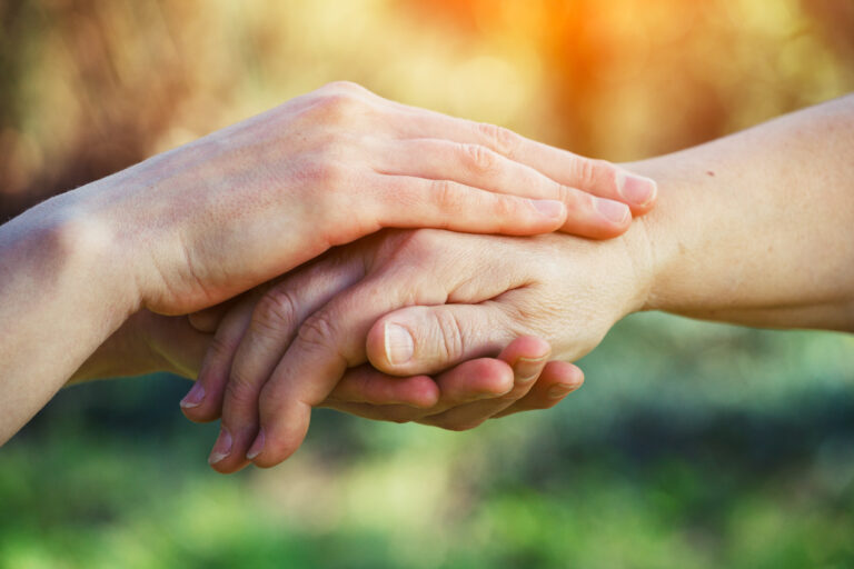 A caretaker holds the hand of an elderly patient who is receiving hospice care at home.