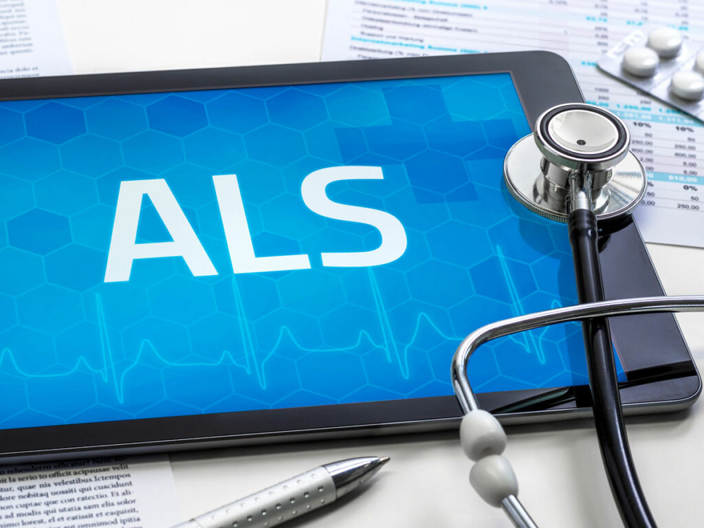 ALS Management Tools: A mobile phone displaying 'ALS' on a physician's desk, alongside a pill pack and stethoscope, for comprehensive care.