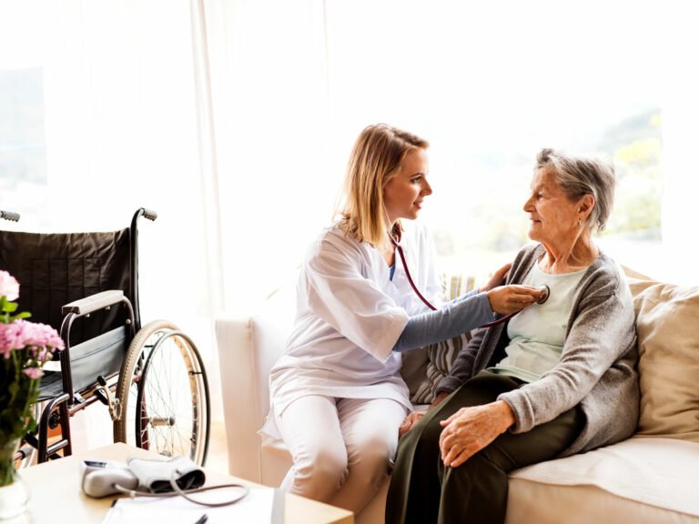 At-Home Comfort Care: A female patient receives attentive care from a female nurse, checking breathing with a stethoscope, reflecting home healthcare.