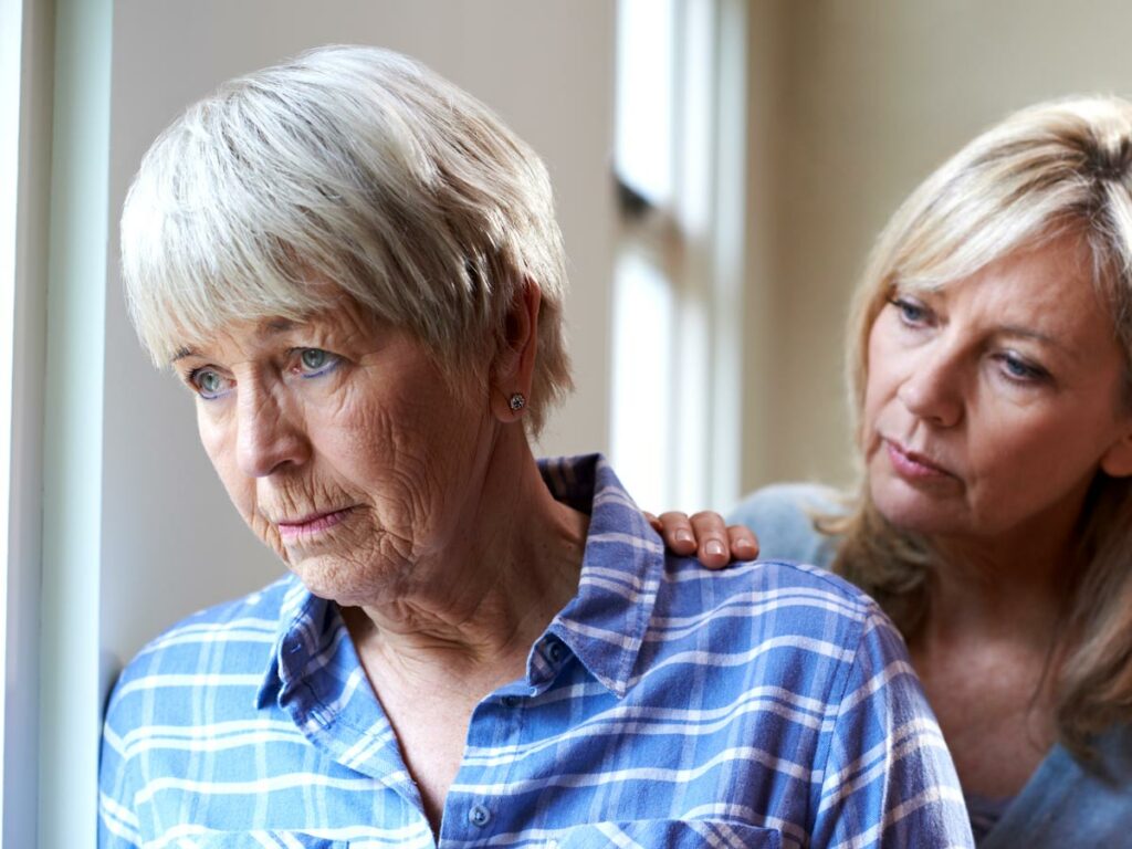 Worried daughter caring for her mother with dementia by the window, demonstrating unconditional love and patience.