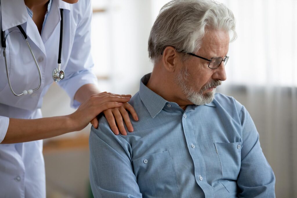 A compassionate healthcare provider comforts an elderly male patient, illustrating the emotional and supportive aspects of pain management.