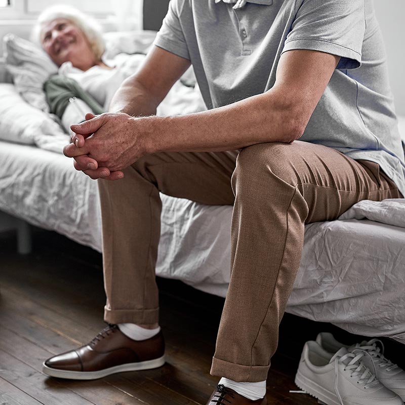 A poignant photograph of an elderly woman lying in bed at the end of life, with a loved one sitting nearby, capturing the emotional connection and moments of holding on in her final days.