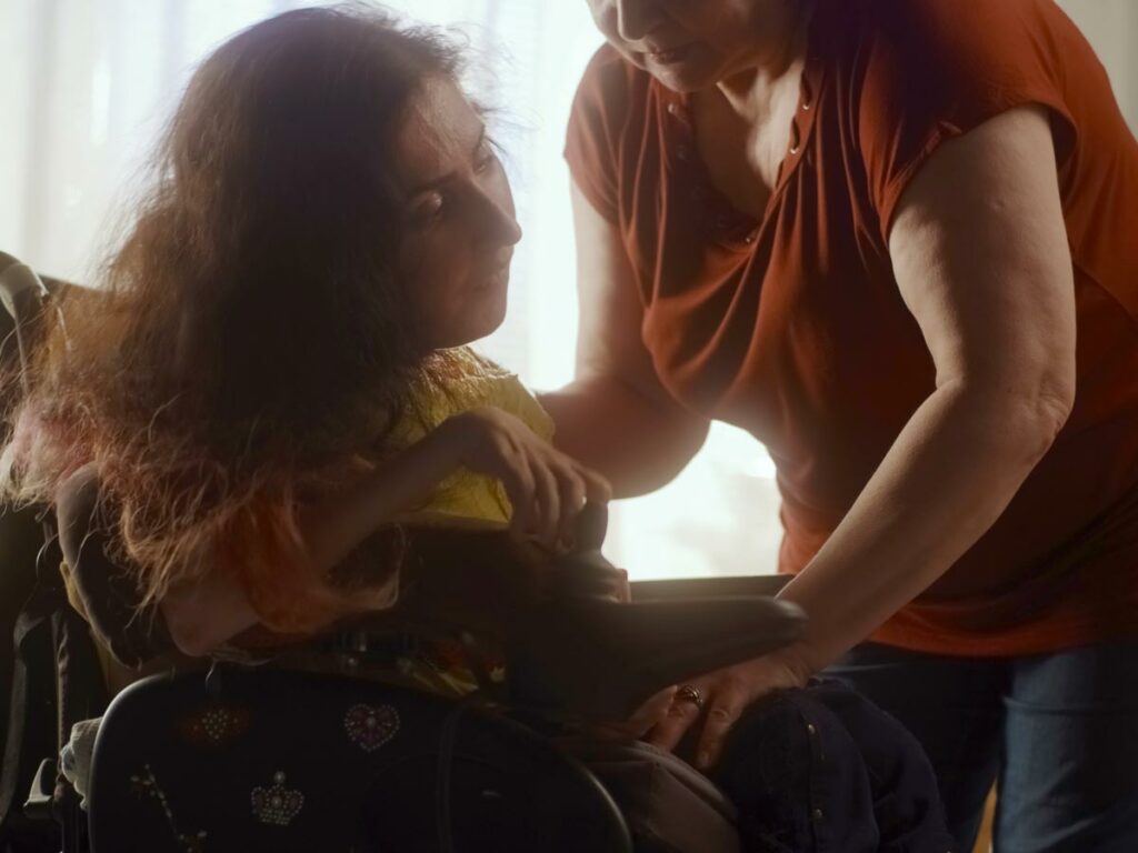 Woman with ALS in a wheelchair, receiving compassionate support from a loved one, sharing a moment of care and resilience.