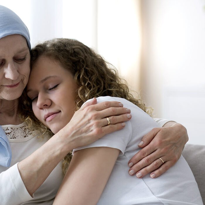Daughter hugging sick elderly mother with cancer wearing a blue headscarf