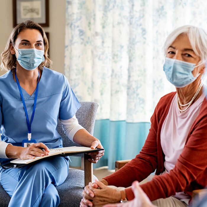 Nurse listening to seniors patients with face mask about covid-19 while being in a home visit. Psychologist during covid19 pandemic wearing surgical mask while visiting senior couple at home. Nurse bringing home the results of medical exams of senior man and woman.