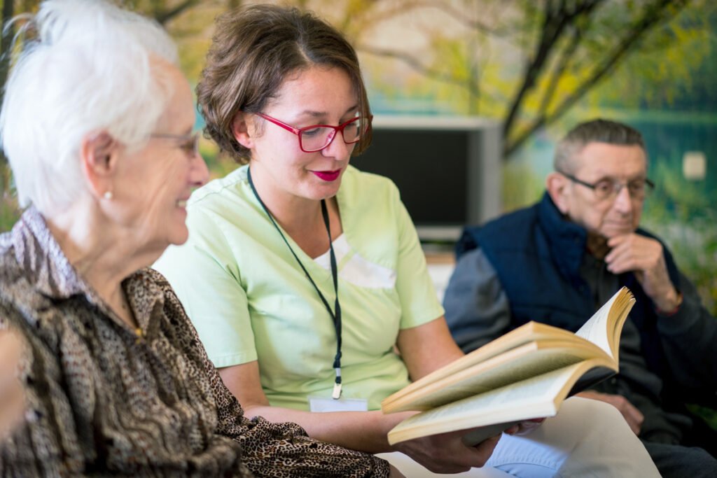In a group home setting, a caring hospice volunteer reads to a patient.