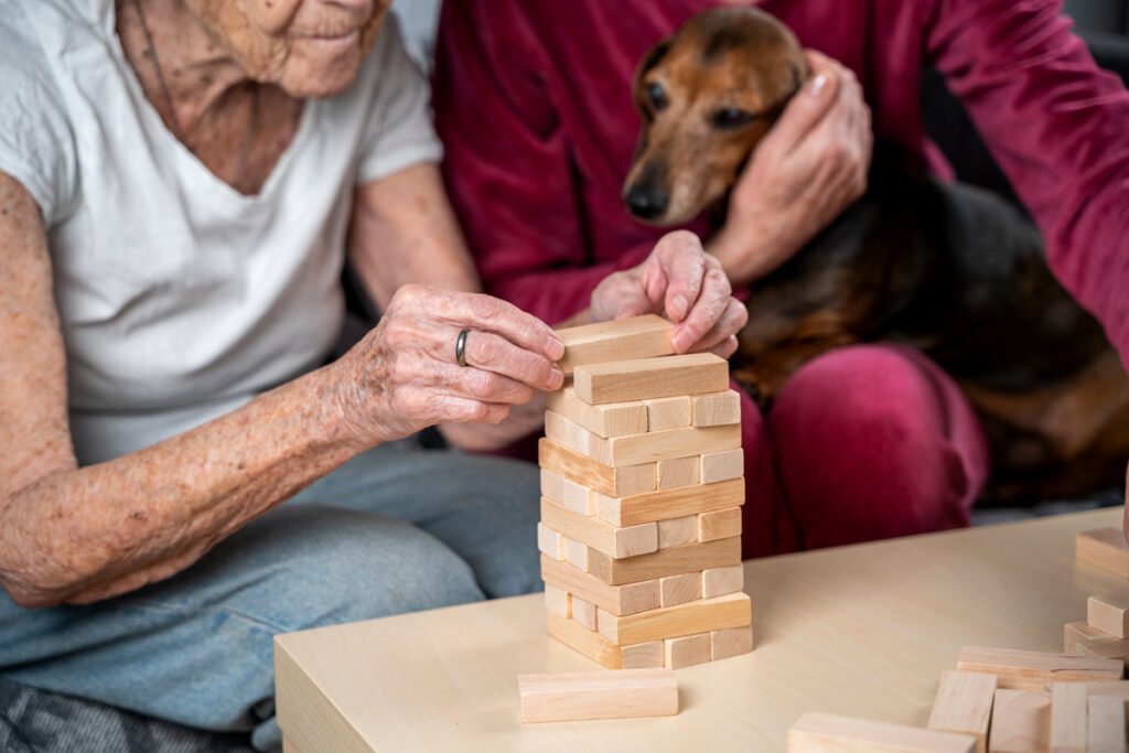 A hospice volunteer cradles a pet dog while a patient prepares to play a game of Jenga.